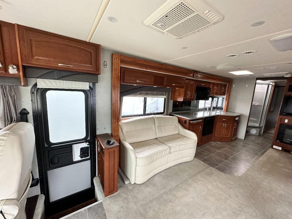 Interior of the 2008 Fleetwood Pace Arrow showing the door, a 2 person couch, kitchen, and peaks of the bathroom in the far back.