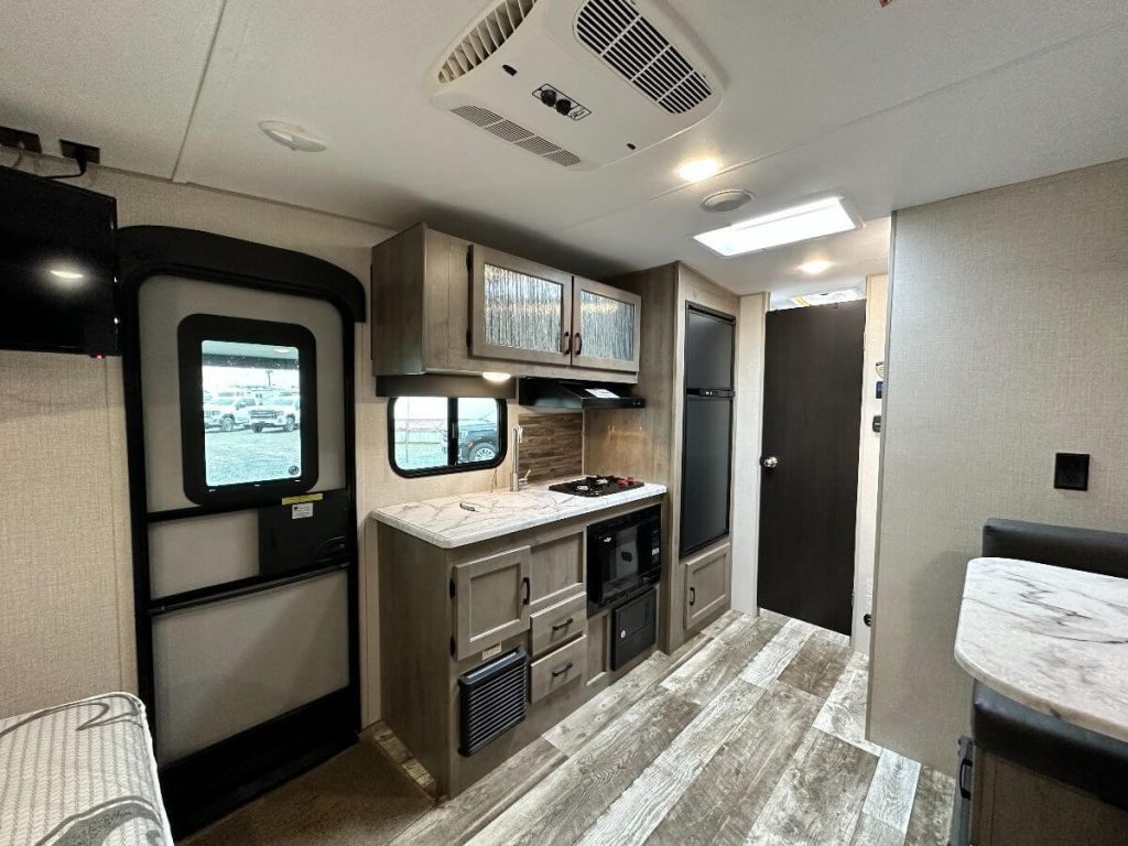 Interior view of RV showing kitchenette, door, and part of the dining area.