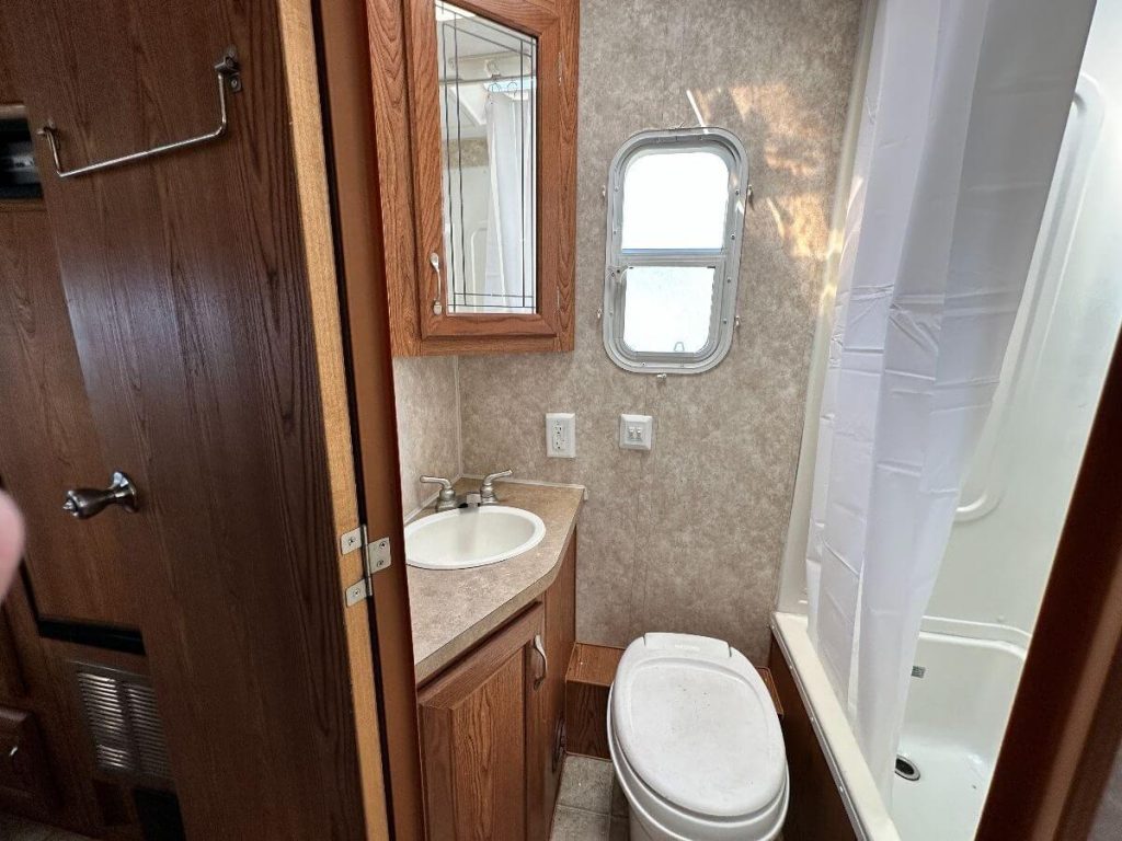Bathroom with toilet, sink, shower, and small window.